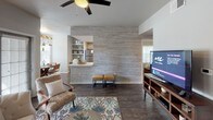This single-story residence offers a well-organized layout encompassing multiple bedrooms, two full bathrooms, a functional kitchen, a dedicated dining area, and a comfortable living room. The living room features dark hardwood-style flooring, a ceiling fan, and a striking textured wood-panel accent wall that visually separates the space from the kitchen. A pass-through opening connects the two areas, enhancing the open flow between them.

The kitchen is appointed with gray cabinetry, speckled quartz-style countertops, stainless steel appliances, and dark hardwood-style flooring. It opens directly into a bright dining nook surrounded by windows with horizontal blinds, lit by a distinctive suspended wood-frame pendant fixture.

The bedrooms each carry their own character: one features a bold teal accent wall with a rustic wood headboard and ceiling fan; another presents a neutral palette with a large window and carpet flooring; a third offers a warm peach accent wall in a cozier setting.

Both bathrooms share a consistent design language, featuring gray cabinetry, vessel sinks, speckled countertops, wide mirrors, dark hardwood-style flooring, and tiled tub-shower combinations with curtains.