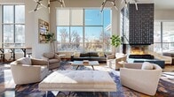 Located at 1291 S Ulster St in Denver, CO, this single-floor clubhouse offers a generously sized, thoughtfully designed communal space ideal for gathering and entertaining. The living room is a standout area, featuring soaring ceilings and expansive floor-to-ceiling windows that flood the interior with natural light and offer views of the surrounding outdoor areas. A striking geometric-textured fireplace serves as a dramatic focal point, complemented by comfortable seating arrangements and a vibrant, abstract-patterned area rug that adds a bold artistic element to the space. Track lighting overhead adds both function and a modern aesthetic. The kitchen is equally impressive, boasting rich wood-grain cabinetry with dark countertops, a large central island with bar-height seating, a professional-grade double wall oven, and a wine cooler. Tall windows bathe the kitchen in natural light, while large-format tile flooring adds a clean, contemporary finish. Open shelving with warm wood tones provides additional character. A glass-enclosed room visible from the living area offers a semi-private space within the clubhouse. Together, these spaces create a welcoming, upscale environment designed for community and convenience.