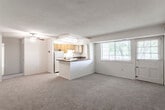 This single-floor residence offers a practical and comfortable layout designed for everyday living. The open-concept living area is spacious and carpeted, creating a warm, cohesive feel throughout. A ceiling fan provides both comfort and a subtle design element overhead, while a textured ceiling adds dimension to the space. Large windows allow natural light to pour in, offering pleasant views of the surrounding greenery.

The kitchen is thoughtfully positioned adjacent to the living area, separated by a peninsula counter with a dark laminate surface that doubles as a casual dining or prep space. Warm honey-toned wood cabinetry lines the walls, providing generous storage, while the kitchen is equipped with a gas range, refrigerator, dishwasher, and a sink positioned beneath a window. The tile flooring in the kitchen offers a clean contrast to the carpeted living spaces.

The bedrooms are well-proportioned and carpeted, each with neutral walls and windows that invite natural light. At least one bedroom features a sliding-door closet with built-in shelving, offering organized storage. Built-in shelving is also visible in the living area, adding functional display space.

The bathroom includes a wood-toned vanity with a white basin sink, a mirrored medicine cabinet, and overhead lighting, keeping the space clean and utilitarian. Overall, the residence presents a straightforward, functional design with comfortable, livable interiors throughout.