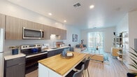 This single-floor studio is designed with a contemporary open-plan layout that seamlessly integrates the kitchen, dining, and living areas into one cohesive space. The kitchen is a standout feature, outfitted with a full suite of stainless steel appliances — including a refrigerator, electric range, over-the-range microwave, and dishwasher — complemented by two-tone cabinetry in warm wood and dark charcoal tones. Light quartz countertops and an undermount sink add a clean, modern finish. A central island with a warm butcher block top and bar seating serves as both a functional prep area and a casual dining spot.

Light wood-tone flooring runs throughout, lending warmth and visual continuity across the entire space. The living area is generously proportioned and benefits from abundant natural light streaming through large sliding glass doors that open to an outdoor patio, offering pleasant outdoor views. Recessed lighting throughout ensures well-lit interiors at any hour.

The bathroom is clean and functional, featuring a full soaking tub with a shower, light wood-tone flooring, and a vanity with ample counter space. Crisp white walls and modern fixtures give the room a fresh, neutral aesthetic. Overall, the space delivers a bright, well-appointed, and efficiently designed living environment suited to modern urban living.