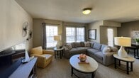 Located along the I-35 service road in Moore, Oklahoma, this single-story unit offers a practical and comfortable layout designed for everyday living. The living room serves as the central gathering space, featuring plush carpeting, neutral-toned walls, and multiple windows fitted with horizontal blinds that allow generous natural light to fill the room. A textured ceiling and flush-mount lighting complete the relaxed atmosphere.

The kitchen is a standout area, outfitted with rich dark cabinetry, bold granite-style countertops, and tile flooring. A peninsula counter provides additional prep and serving space, while stainless steel appliances—including a refrigerator with ice and water dispenser, range, and microwave—add a modern, functional touch. Ample upper and lower cabinet storage enhances the kitchen's utility.

The bathroom continues the dark cabinetry theme, featuring a granite-topped vanity, a large mirror with decorative lighting above, and dark tile flooring. A full shower-tub combo with tiled surround and curtain enclosure completes the space. The bedroom, visible in the 3D scan, accommodates a full furniture arrangement with a window providing natural light. Overall, the unit presents a cohesive, neutral design palette throughout.