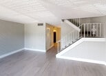 Located at 3901 36th Ct in West Palm Beach, Florida, this two-story residence offers a well-organized layout with updated finishes throughout. The main living area on the first floor features light gray wood-look tile flooring, a distinctive shiplap accent wall with a diagonal pattern, and a textured ceiling. A white metal staircase leads to the upper level, while a louvered closet door provides convenient storage access nearby.

The kitchen is outfitted with white flat-front cabinetry, a dark subway tile backsplash, black appliances including a range and refrigerator, and an in-unit washer — offering both style and practicality. Multiple living and bedroom spaces are spread across both floors, each finished with the same durable wood-look tile flooring and neutral gray walls. Bedrooms include closets with bifold doors and windows that bring in natural light and outdoor views of the surrounding neighborhood.

The bathroom features gray marble-style wall tile surrounding a full tub-shower combination, complemented by a vanity with a light stone-top and coordinating tile flooring. A sliding glass door on the upper level opens to an outdoor balcony, extending the living space and providing views of the lush greenery outside. The overall aesthetic is clean, modern, and move-in ready.