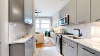 Located at 222 West Blvd in Charlotte's vibrant South End neighborhood, this single-floor residence offers a thoughtfully designed layout with contemporary finishes throughout. The kitchen is a standout feature, outfitted with flat-front gray cabinetry, a geometric herringbone tile backsplash, white quartz countertops, stainless steel appliances including a French door refrigerator, electric range, and over-the-range microwave. The kitchen flows seamlessly into the open living area, which is brightened by large windows and finished with a ceiling fan overhead. The bedroom is generously sized and bathed in natural light from oversized windows that frame urban skyline views. It includes a walk-in closet with sliding doors and ample storage. The bathroom is finished with striking dark penny-round tile in the shower and tub surround, contrasting elegantly with light wood-look flooring, a gray vanity with a white countertop, matte black fixtures, and a mirrored medicine cabinet. Light, neutral tones and consistent modern hardware tie the entire space together, creating a clean and cohesive aesthetic that balances style with everyday functionality.