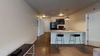 This single-floor unit offers a functional and cohesive layout designed for comfortable everyday living. The open-concept kitchen and living area serves as the central hub of the space, anchored by a peninsula-style counter with a granite surface and bar seating for two. Dark cabinetry pairs with black appliances, including a refrigerator, range, and built-in microwave, while pendant lighting above the counter adds a modern touch. The kitchen flows naturally into the living area, creating an interconnected space well-suited for both relaxing and entertaining.

Dark hardwood-style flooring runs consistently throughout the unit, lending a clean, uniform aesthetic. A hallway connects the main living area to the two bedrooms, each featuring a window with blinds that allows natural light to filter in, neutral-toned walls, and continued hardwood-style flooring. Both bedrooms offer a quiet, understated atmosphere with straightforward, practical proportions.

The unit includes two full bathrooms, each equipped with a tub-shower combination, toilet, and a dark-cabinetry vanity with a granite countertop. The bathrooms maintain the same neutral color palette found throughout the unit, contributing to an overall sense of consistency and simplicity across the entire space.
