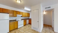 Located at 2140 N Zaragoza Rd in El Paso, TX, this efficient single-story unit offers a well-organized layout across a comfortable floor plan. The kitchen is a standout functional space, featuring warm honey-toned wood cabinetry with ample upper and lower storage, dark granite-style countertops, light ceramic tile flooring, and a full suite of white appliances including a refrigerator, electric range, and dishwasher. A dedicated floor vent and under-cabinet range hood add practical utility to the space.

The bedroom is a calm, carpeted retreat bathed in natural light from a window overlooking the outdoors. Neutral white walls and plush beige carpet create a clean, comfortable atmosphere. An adjacent walk-in closet provides generous storage with dual hanging rods along both walls and additional shelving, all finished with the same carpet underfoot.

The bathroom is straightforward and functional, featuring a tiled tub-shower combination with a chrome shower rod, a wall-mounted wood vanity cabinet, and tile flooring consistent with the kitchen. The overall design of the unit is simple and clean, with white walls throughout, providing a neutral canvas that is easy to personalize.