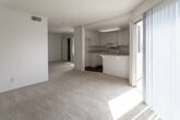Located at 1256 W Arrow Hwy in Upland, California, this single-floor unit offers a straightforward and functional layout spread across an open, connected living space. The main living area is generously proportioned, featuring light-toned carpeting and a textured ceiling that runs throughout. A sliding glass door allows natural light to pour in while providing access to the outdoors. The kitchen is positioned adjacent to the living area and features white cabinetry with ample upper and lower storage, light speckled countertops, and a full suite of white appliances including an electric range, over-the-range microwave, and dishwasher. A double-basin sink sits beneath a window, adding natural light to the workspace. The kitchen floor is finished in warm hardwood-style flooring, which also extends into the bathroom. The bedroom is spacious and carpeted, offering a sliding-door closet with built-in shelving and an adjacent vanity or dressing area. The bathroom is clean and simply appointed, featuring a full soaking tub with shower, wood-style flooring, and bright white walls. Central HVAC vents are present throughout, ensuring year-round comfort. The unit presents a clean, neutral palette throughout, making it a versatile and move-in ready space.