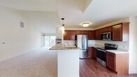 This single-floor residence offers a thoughtfully designed open-concept layout that seamlessly connects the kitchen and living area. The kitchen is a standout feature, equipped with rich cherry wood cabinetry, granite countertops, a central island with a built-in sink, pendant lighting, and a full suite of stainless steel appliances including a French door refrigerator, electric range, microwave, and dishwasher. Wood-look flooring grounds the kitchen, while plush carpet extends throughout the living and bedroom areas.

Vaulted ceilings throughout the residence lend an airy, expansive feel to the space. The living area benefits from a sliding glass door that opens to a private balcony, allowing abundant natural light to fill the room. The bedrooms are generously sized, each featuring vaulted or pitched ceilings, large windows with outdoor views, and ample closet space with paneled doors.

Two bathrooms serve the residence: one features a gray vanity, white countertop, tile flooring, and a glass-door shower, while the second offers a warm wood vanity and tile flooring. A dedicated laundry room with a full-size Whirlpool washer and dryer, overhead cabinetry, and a wall-mounted shelf rack adds everyday convenience to this well-rounded home.