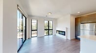 Located at 1312 John Q Hammons Dr in Middleton, WI, this contemporary 2-bedroom, 2-bathroom unit offers a thoughtfully designed open-concept floor plan. The living area features light wood-look flooring and a sleek built-in fireplace that serves as a striking focal point, seamlessly connecting to the kitchen. The kitchen is well-appointed with dark wood cabinetry, granite countertops, stainless steel appliances including a range, microwave, and refrigerator, a white quartz island with a double sink, and pendant lighting overhead. A sliding glass door leads out to a private balcony with outdoor views, and large black-framed windows throughout the unit flood the space with natural light. The spacious primary bedroom features plush carpeting, a ceiling fan, and generous windows with outdoor views, while the second bedroom is similarly finished with carpet and a ceiling fan. Both bathrooms are finished with dark wood vanities, granite countertops, and neutral tile flooring. A dedicated closet provides additional storage. The clean, modern aesthetic is carried throughout with crisp white walls and contemporary fixtures, creating a bright and cohesive living environment.