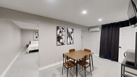 This modern studio in Lexington, Kentucky, offers a well-planned single-floor layout that maximizes every square foot through thoughtful design and a clean, minimalist aesthetic. The interior is finished in neutral grey tones throughout, with smooth light-colored flooring and crisp white trim that creates a cohesive and airy feel.

The main living area seamlessly combines sleeping and lounge functions, featuring a full bed accompanied by a sectional sofa and a patterned area rug, all accented by equestrian-themed wall art that adds a nod to the local culture. A wall-mounted flat-screen television and a dedicated workspace with a desk and chair provide both entertainment and productivity options. An open wardrobe unit offers convenient clothing storage. Recessed ceiling lighting and a wall-mounted mini-split HVAC unit ensure year-round comfort.

The dining area is defined by a wooden table with seating for four, flanked by abstract black-and-white artwork, and is illuminated by recessed overhead lighting. A compact kitchenette is tucked efficiently into one end of the space, equipped with essential appliances.

The bathroom maintains the studio's minimalist style, featuring a wall-mounted white basin with matte black fixtures, white subway tile, a frameless mirror, and sleek industrial-style shelving for towel and toiletry storage.