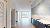 Located on N Milwaukee Ave in Chicago's vibrant Logan Square neighborhood, this single-floor unit showcases a clean, contemporary design throughout. Light-toned hardwood flooring runs continuously across the open-concept living and kitchen areas, creating a cohesive and airy feel. The living space is generously proportioned, with neutral walls and ample room for flexible furniture arrangements. Large floor-to-ceiling windows at the far end of the living area flood the space with natural light and offer views of the surrounding cityscape.

The kitchen is well-appointed, featuring a two-toned cabinet design that pairs dark wood lower cabinetry with lighter upper cabinets. White subway tile backsplash, stainless steel appliances including a gas range, microwave, refrigerator, and dishwasher, along with sleek countertops, complete the functional and stylish kitchen. A closet with built-in shelving provides convenient storage near the entry.

The bathroom is finished in a modern style, with a large-format dark tile floor, a deep soaking tub with a sliding glass enclosure and white subway tile surround, a rectangular undermount sink with chrome fixtures, and a wide vanity mirror with a contemporary wall sconce. Rail lighting throughout the unit adds a polished, gallery-like aesthetic.