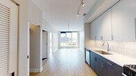 Located on N Milwaukee Ave in Chicago's vibrant Logan Square neighborhood, this single-floor unit showcases a clean, contemporary design throughout. Light-toned hardwood flooring runs continuously across the open-concept living and kitchen areas, creating a cohesive and airy feel. The living space is generously proportioned, with neutral walls and ample room for flexible furniture arrangements. Large floor-to-ceiling windows at the far end of the living area flood the space with natural light and offer views of the surrounding cityscape.

The kitchen is well-appointed, featuring a two-toned cabinet design that pairs dark wood lower cabinetry with lighter upper cabinets. White subway tile backsplash, stainless steel appliances including a gas range, microwave, refrigerator, and dishwasher, along with sleek countertops, complete the functional and stylish kitchen. A closet with built-in shelving provides convenient storage near the entry.

The bathroom is finished in a modern style, with a large-format dark tile floor, a deep soaking tub with a sliding glass enclosure and white subway tile surround, a rectangular undermount sink with chrome fixtures, and a wide vanity mirror with a contemporary wall sconce. Rail lighting throughout the unit adds a polished, gallery-like aesthetic.