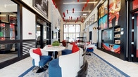 This striking single-floor lounge is designed with a bold, contemporary aesthetic that immediately captures attention. A red, white, and blue color palette runs throughout the space, reflected in the plush seating arrangements featuring curved white chairs and deep blue accent seats adorned with vivid red cushions. Sleek round tables anchor intimate seating clusters, creating a social yet comfortable atmosphere.

The ceiling is a standout architectural feature, showcasing a dynamic installation of suspended red geometric blocks alongside linear lighting elements that draw the eye upward and add dramatic depth to the room. The flooring features an intricate patterned carpet that complements the overall design scheme with its flowing, organic motifs.

Large floor-to-ceiling windows along the far wall flood the interior with natural light, offering views to the outdoors and reinforcing the open, airy ambiance. The walls are adorned with large-format framed artwork and oversized display screens, adding a multimedia dimension to the space. Dark-framed glass partitions define areas within the lounge while maintaining a sense of openness. The combination of vibrant colors, curated artwork, statement lighting, and thoughtful furnishings gives this space an energetic yet welcoming character suited for gathering and socializing.