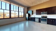 Rayette Lofts Unit 606 is a one-bedroom, one-bathroom loft that masterfully blends industrial character with modern conveniences. The open-concept living and kitchen area is defined by striking corrugated metal ceilings and smooth polished concrete floors, creating a spacious, airy atmosphere with authentic loft appeal. Exposed ductwork and track lighting add to the industrial aesthetic throughout.

The kitchen is well-appointed with rich dark cabinetry, light countertops, a textured tile backsplash, and a full suite of stainless steel appliances including a refrigerator, range, built-in microwave, and dishwasher. Large, multi-pane industrial-style windows flood the living area with abundant natural light while offering views of the surrounding urban landscape.

The bathroom features dark cabinetry consistent with the kitchen's design, a vanity with light countertop, and tile flooring. A dedicated laundry area includes a stacked washer and dryer unit alongside a walk-in closet with wire shelving, providing practical in-unit storage. The bedroom area offers generous wall space and continues the polished concrete flooring found throughout. This unit delivers a distinctive urban living experience rooted in thoughtful, industrial-inspired design.
