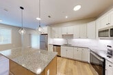 Located at 150 Draper Ave in North Attleborough, MA, this well-appointed single-floor residence offers three bedrooms, two bathrooms, and a thoughtfully designed layout. The kitchen is a standout feature, showcasing white shaker-style cabinetry, a subway tile backsplash, granite countertops, a central island with pendant lighting, and a full suite of stainless steel appliances including a refrigerator, range, microwave, and dishwasher. Light hardwood flooring flows consistently throughout the home, creating a cohesive and clean aesthetic. The living area benefits from natural light through a large sliding glass door fitted with vertical blinds, which opens directly to a private patio. Both bathrooms echo the kitchen's refined style with granite-topped white vanities and hardwood flooring. The bathrooms include a walk-in shower. The bedrooms are bright and neutral, with windows allowing ample natural light and generous closet space — six closets total are distributed throughout the home. Additional practical spaces include a dedicated laundry room and a utility room. Recessed lighting throughout complements the home's modern, move-in-ready appeal.