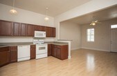 This single-floor unit is thoughtfully laid out to maximize functionality and comfort. The main living area greets occupants at the front entry, which features a white panel door with a transom window allowing natural light to filter in. Light wood laminate flooring extends throughout the living and kitchen spaces, lending a clean, cohesive appearance. A ceiling fan and electrical panel are also present in the main living area.

The kitchen is designed in a U-shaped configuration and opens to the living space via a raised breakfast bar counter. Rich, dark cherry-toned cabinetry lines the walls from counter to ceiling, providing generous storage. White appliances, including a range, microwave, dishwasher, and refrigerator, complement the neutral countertops. Pendant and flush-mount ceiling lights illuminate the workspace effectively.

The bedroom is carpeted in a warm tan tone, offering a comfortable contrast to the hard flooring in the rest of the unit. It includes a dedicated walk-in closet with a hanging rod, as well as an additional double-door closet, providing ample storage.

The bathroom features terracotta-toned tile flooring, a dark wood vanity with storage, a toilet, and a full tub-shower combination with white surround, completing the unit's practical amenities.