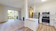 Located in the Mira Mesa neighborhood of San Diego, this single-floor residence offers a well-designed layout that balances comfort and modern finishes throughout. The open-concept living and dining area features plush carpeting, soaring ceilings, and a tiled fireplace that serves as a focal point of the room. Sliding glass doors lead to a private balcony overlooking lush, mature trees, bringing abundant natural light into the space.

The kitchen is thoughtfully designed with crisp white cabinetry, stainless steel appliances including a refrigerator, electric range, and microwave, and a marble-style countertop peninsula that provides additional prep space and a natural divide from the living area. Light wood-style flooring ties the kitchen and entry areas together seamlessly.

The bedrooms are generously sized, with soft carpeting, bright windows framing peaceful greenery views, and ample closet space, including a walk-in closet in the primary bedroom. The bathroom is clean and modern, featuring a marble-style vanity countertop, undermount sink, light wood cabinetry, a large mirror, and a shower-tub combination. The overall aesthetic of the home is bright and neutral, creating a calm and inviting atmosphere throughout.
