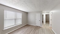 This 3-bedroom, 1-bathroom unit in Lexington, KY offers a practical and well-organized single-floor layout. Neutral gray walls and light-toned luxury vinyl plank flooring flow throughout the main living areas, creating a clean, cohesive aesthetic. The living room features a ceiling fan, chair-rail molding, and natural light from blinds-fitted windows. The kitchen is efficiently designed with white cabinetry, granite-style countertops, a subway tile backsplash, black appliances including a range and refrigerator, and an under-cabinet range hood. All three bedrooms are carpeted and feature ceiling fans, with windows providing natural light. The primary bedroom includes a closet with built-in shelving and rod. The shared full bathroom is appointed with a tub/shower combination, white tile surround, a vanity with white cabinetry, and oil-rubbed bronze fixtures. Wall-mounted AC units are present in select rooms. Textured ceilings are consistent throughout, and clean white trim and baseboards provide a polished finish across the entire unit. A connecting hallway ties all rooms together in a straightforward, functional floor plan.