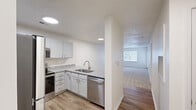 Located at Trellis Pointe in Holly Springs, NC, this two-bedroom, one-bathroom residence offers a well-designed single-floor layout that maximizes functionality and comfort. The kitchen is a standout feature, equipped with stainless steel appliances including a refrigerator, range, microwave, and dishwasher, all complemented by crisp white shaker-style cabinetry and granite countertops. Wood-look flooring runs throughout the kitchen and flows into a peninsula that opens toward the living area, creating a seamless connection between spaces. The living room is generously proportioned, featuring plush carpeting, a textured ceiling, and windows alongside a glass door that invite natural light and provide outdoor access. The primary bedroom is a comfortable retreat with carpeted flooring, a ceiling fan with light fixture, and a window that brings in natural light. The second bedroom also features carpeting and a window, offering a bright and versatile space. The bathroom includes a full tub-shower combination and wood-look tile flooring, maintaining a clean and consistent aesthetic throughout. A dedicated laundry area with hookups adds everyday convenience to this well-appointed Holly Springs residence.