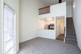 Located in Walnut Creek, CA, this two-story, one-bedroom, one-bathroom home offers a smart and efficient layout spread across two floors. The main level features a soaring vaulted ceiling in the living and dining area, creating an airy, open atmosphere that feels larger than its footprint suggests. Large windows with slatted blinds line the living room walls, inviting abundant natural light and offering views of the surrounding neighborhood. A wall-unit air conditioner and an exterior door provide both comfort and convenient access. The open-concept kitchen is positioned on a raised platform visible from the living area, outfitted with white cabinetry, stainless steel appliances including a refrigerator and microwave, and a breakfast bar-style counter. A staircase with a distinctive red railing leads from the main level to the upper floor, where the private bedroom is situated. The bedroom features plush carpeting and a large window with blinds that filters in soft, natural light. Three closets throughout the home provide generous storage. The full bathroom is finished with wood-look tile flooring, a combined tub and shower with sliding glass doors, a toilet, and a single-sink vanity with a light countertop. The overall aesthetic is clean, bright, and neutral throughout.