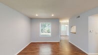 This two-floor residence offers a clean, functional layout with thoughtful finishes throughout. The main living areas feature warm hardwood-style flooring that flows seamlessly from the spacious living room into the dining area, where a pendant light fixture and a pass-through opening connect to the kitchen. Natural light pours in through multiple windows fitted with blinds, providing pleasant views of surrounding greenery. Recessed lighting in the living area adds a modern touch to the textured ceiling above.

The kitchen is well-equipped with rich dark cabinetry, stone-look countertops, a double-basin sink, and stainless steel appliances including a dishwasher and refrigerator. Track lighting illuminates the workspace efficiently.

The bedrooms are carpeted for comfort and each features a window with outdoor views, offering a quiet and bright retreat. The bathrooms are finished with wood-look flooring, dark vanity cabinetry, and brushed nickel fixtures. The full bathroom includes a tub-shower combination, while a second bathroom presents a compact half-bath layout with a sloped ceiling detail, adding architectural character.

Throughout the space, a consistent soft gray-blue palette on the walls creates a calm, cohesive atmosphere that complements the varied flooring materials and darker accents found in the kitchen and bathrooms.