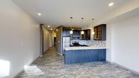 This well-appointed 2-bedroom, 2-bathroom single-floor residence offers a thoughtfully designed open-concept layout that maximizes both functionality and style. The kitchen serves as the heart of the home, showcasing dark espresso cabinetry with open display shelving, a mosaic tile backsplash, and a full suite of stainless steel appliances including a refrigerator, range, and built-in microwave. A generous kitchen island with a crisp white countertop provides additional prep space and casual seating, while three pendant lights hang above, adding warmth and a contemporary touch. Recessed lighting throughout ensures the space remains bright and welcoming. The durable wood-look flooring flows seamlessly from the kitchen into the open living areas and down the hallway, tying the space together with a cohesive, modern aesthetic. Neutral-toned walls complement the rich cabinetry and allow for flexible interior styling. A long hallway leads to the private areas of the home, including the two bedrooms and bathrooms. The overall ambiance strikes a balance between contemporary design and comfortable everyday living, making this a practical and visually appealing residence.