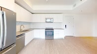 Located at 215 Park in Hallandale Beach, Florida, this single-floor, 3-bedroom, 2-bathroom residence offers a clean, modern aesthetic throughout. The open-concept kitchen is outfitted with flat-front white cabinetry extending to the ceiling, gray quartz countertops, a marble-style tile backsplash, and a full suite of stainless steel GE appliances including a refrigerator, range, over-the-range microwave, and dishwasher. A tray ceiling adds architectural dimension to the kitchen and living area.

Light wood-tone flooring runs throughout the unit, creating a warm, cohesive look. Each bedroom features large black-framed windows that invite generous natural light and frame views of surrounding green recreational fields and the broader Hallandale Beach skyline. Ceiling fans are present in the bedrooms for added comfort.

Both bathrooms are finished to a high standard, showcasing marble-look porcelain tile on the floors and shower surrounds, tub-shower combinations enclosed by sliding glass doors, white undermount sinks set into wood-grain floating vanities, and backlit LED mirrors that lend a sleek, contemporary feel. The overall ambiance of the unit is bright, clean, and move-in ready.