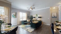 This single-floor residence showcases a thoughtfully designed layout with distinct living spaces, each finished with dark hardwood-style flooring and neutral gray walls that create a cohesive, contemporary aesthetic throughout.

The living room is a standout space, featuring crown molding, a ceiling fan, and natural light from windows dressed with sheer drapes and wood blinds. Bold emerald green velvet seating with gold accents is anchored by a vibrant abstract area rug, complemented by a sleek gold credenza and colorful wall art, creating a refined yet inviting atmosphere.

The dining area accommodates a glass-top table with upholstered chairs and benefits from generous window light and large-scale abstract artwork. The kitchen features white shaker cabinetry, a marble-look tile backsplash, dark granite countertops, and stainless steel appliances.

The bedrooms include a softly styled nursery with crown molding and ample natural light, and an additional bedroom with a charming, feminine aesthetic. A full bathroom includes a soaking tub with marble surround, dark granite vanity countertops, and white cabinetry, completing the home's polished interior presentation.