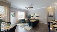 This single-floor residence showcases a thoughtfully designed layout with distinct living spaces, each finished with dark hardwood-style flooring and neutral gray walls that create a cohesive, contemporary aesthetic throughout.

The living room is a standout space, featuring crown molding, a ceiling fan, and natural light from windows dressed with sheer drapes and wood blinds. Bold emerald green velvet seating with gold accents is anchored by a vibrant abstract area rug, complemented by a sleek gold credenza and colorful wall art, creating a refined yet inviting atmosphere.

The dining area accommodates a glass-top table with upholstered chairs and benefits from generous window light and large-scale abstract artwork. The kitchen features white shaker cabinetry, a marble-look tile backsplash, dark granite countertops, and stainless steel appliances.

The bedrooms include a softly styled nursery with crown molding and ample natural light, and an additional bedroom with a charming, feminine aesthetic. A full bathroom includes a soaking tub with marble surround, dark granite vanity countertops, and white cabinetry, completing the home's polished interior presentation.