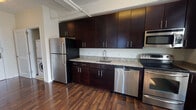 Located at 425 Monmouth St in Jersey City, NJ, this single-floor unit offers a thoughtfully designed layout that balances modern finishes with functional living spaces. The kitchen is a standout feature, showcasing rich dark espresso cabinetry extending floor to ceiling, granite countertops, a stainless steel sink, and a full suite of stainless steel appliances including a refrigerator, dishwasher, microwave, and range. Exposed overhead piping adds an industrial loft-like character to the space. Rich hardwood flooring runs throughout the main living and kitchen areas, lending warmth and continuity. The bedroom is bright and inviting, benefiting from natural light streaming through a large window with urban views of the surrounding cityscape, complemented by the same elegant hardwood floors. The full bathroom is finished with light tile flooring, a dark-cabinet vanity with a wide mirror and vanity lighting, and a combined tub and shower enclosed by sliding glass doors. A generously sized walk-in closet with built-in wire shelving and hanging rods provides ample storage. In-unit laundry is also present, adding convenience to everyday living.