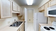 This single-story residence features a neutral, light-filled interior with a practical and cohesive layout throughout. The galley-style kitchen is efficiently designed with light wood cabinetry offering ample storage, a double stainless steel sink, light-toned countertops, white appliances including a refrigerator and electric range, and white tile flooring underfoot. A pendant light fixture highlights the adjacent dining area, which opens directly to the living room, creating a connected flow between the spaces. The living room features rich, dark hardwood flooring, a textured ceiling, a ceiling fan with light kit, and wide sliding windows dressed with vertical blinds that allow natural light to fill the room.

The bedrooms are carpeted for comfort and each includes a ceiling fan, vertical blinds, and windows that bring in natural light. One bedroom includes two doors, offering access to both a hallway and a closet. The two bathrooms share a consistent design, each featuring a tub-shower combination with tiled surrounds, a toilet, a single vanity with a light wood cabinet base, and a wall-mounted mirror. The overall palette throughout the unit is warm beige and cream, contributing to a clean, functional ambiance.
