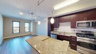 Located in the Columbia Heights neighborhood of Washington, DC, this 1-bedroom, 2-bathroom residence offers a thoughtfully designed open-concept layout with contemporary finishes throughout. The kitchen and living room share an open, flowing space anchored by a granite-topped center island with pendant lighting overhead. The kitchen is outfitted with rich dark-wood cabinetry extending to the ceiling, stainless steel appliances including a gas range, built-in microwave, dishwasher, and refrigerator, all complemented by granite countertops and wood-look flooring. Track lighting adds a modern touch to the combined living and kitchen area, which is brightened by windows offering city views. The bedroom is a comfortable and well-proportioned retreat featuring plush carpeting, dual windows that invite natural light and provide elevated neighborhood views, and a clean, neutral color palette. Two full bathrooms serve the residence, providing added convenience. Additional spaces include a dedicated closet and a connecting hallway that efficiently links each room. Clean lines, neutral tones, and quality materials define the overall aesthetic, creating a modern and functional living environment in a prime Washington, DC location.