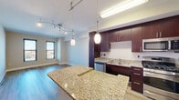 Located in the Columbia Heights neighborhood of Washington, DC, this 1-bedroom, 2-bathroom residence offers a thoughtfully designed open-concept layout with contemporary finishes throughout. The kitchen and living room share an open, flowing space anchored by a granite-topped center island with pendant lighting overhead. The kitchen is outfitted with rich dark-wood cabinetry extending to the ceiling, stainless steel appliances including a gas range, built-in microwave, dishwasher, and refrigerator, all complemented by granite countertops and wood-look flooring. Track lighting adds a modern touch to the combined living and kitchen area, which is brightened by windows offering city views. The bedroom is a comfortable and well-proportioned retreat featuring plush carpeting, dual windows that invite natural light and provide elevated neighborhood views, and a clean, neutral color palette. Two full bathrooms serve the residence, providing added convenience. Additional spaces include a dedicated closet and a connecting hallway that efficiently links each room. Clean lines, neutral tones, and quality materials define the overall aesthetic, creating a modern and functional living environment in a prime Washington, DC location.