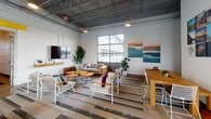 Located at 1125 Commerce Rd in Richmond, Virginia, this single-floor amenity space blends industrial architecture with contemporary design to create a dynamic and inviting environment. Soaring exposed ceilings with steel trusses and open ductwork give the space an airy, loft-like character throughout.

The fitness area is equipped with a row of Life Fitness treadmills featuring integrated display screens, set against a mirrored wall that visually expands the space. Industrial-style lighting and polished concrete floors reinforce the modern aesthetic.

The kitchen and dining area serves as a true centerpiece, anchored by a striking marble island with warm wood-and-metal bar seating. A large-scale landscape mural depicting a serene river scene dominates the back wall, complemented by dark cabinetry and matching marble countertops — creating an artistic and functional gathering space.

The lounge area features comfortable gray sofas, accent chairs, and organic-shaped wooden coffee tables arranged on layered patterned rugs. A wall-mounted flat-screen TV and lush potted palms enhance the relaxed atmosphere, while large steel-framed windows flood the space with natural light and offer views of the surrounding courtyard.

The game room offers a full-size billiards table as its focal point, alongside a workstation nook and additional greenery, all bathed in natural light from expansive industrial windows — rounding out a well-appointed, community-focused space.