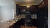 Located at 6667 Wesbury Park Ave in Columbus, Ohio, this single-floor residence offers a thoughtfully designed layout with a clean, contemporary aesthetic throughout. The kitchen is a standout feature, boasting rich dark espresso cabinetry that extends to the ceiling for ample storage, granite-look countertops, a stainless steel double sink, and a full suite of black Whirlpool appliances including an electric range, over-the-range microwave, and refrigerator. A textured tile backsplash adds visual depth, while warm wood-look vinyl flooring grounds the space. A half-wall peninsula seamlessly connects the kitchen to the open living area, which features neutral carpet and easy access to the entryway. The bedrooms are generously sized, each finished with plush neutral carpet and large windows with blinds that allow natural light to fill the rooms. Accent walls in deep charcoal and gray tones add a modern design element to the sleeping areas. The bathroom features wood-look vinyl flooring and clean, neutral gray walls, maintaining the consistent design language found throughout the home. The overall ambiance is modern and understated, offering a functional and comfortable living environment.