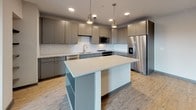 Located at 1005 W Main St in Durham, NC, this modern single-floor unit offers a thoughtfully designed layout with contemporary finishes throughout. The kitchen serves as a standout centerpiece, featuring flat-front cabinetry in a warm gray tone, a classic white subway tile backsplash, quartz countertops, and a generous central island with pendant lighting overhead. Stainless steel appliances — including a refrigerator with ice maker, dishwasher, built-in microwave, and range — complete the well-appointed space. Wood-look plank flooring runs consistently throughout the unit, lending warmth and visual continuity from room to room. The living area is open and bright, with large windows that invite natural light and offer views of the surrounding neighborhood. Bedrooms are comfortably sized, with one featuring a ceiling fan and windows with exterior views. The bathrooms are finished with white subway tile, quartz vanity tops, gray cabinetry, and wood-look flooring — one includes a soaking tub with shower, while another features a walk-in tile shower with glass enclosure. A dedicated laundry room with a full-size side-by-side washer and dryer adds everyday convenience. The overall aesthetic is clean, modern, and cohesive.