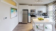Located at 77 H St NW in Washington, DC, this well-appointed one-bedroom apartment offers a thoughtfully designed single-floor layout that balances functionality with modern style. The open-concept living area is filled with natural light from large windows dressed with patterned curtains, offering views of the surrounding urban streetscape. Wood-style flooring runs throughout the main living areas, complemented by track lighting overhead, creating a bright and welcoming ambiance. The living room provides generous space for seating and entertainment, with room for a dining area nearby. The kitchen is efficiently designed with crisp white cabinetry, stainless steel appliances including a refrigerator, electric range, and built-in microwave, along with a gray subway tile backsplash, white countertops, and a stainless steel sink. A movable white kitchen island adds additional prep and storage space. The bedroom is a comfortable retreat featuring plush carpeting, a spacious sliding-door closet, and a narrow window that brings in soft natural light. The bathroom is finished with neutral tile flooring, a tiled tub-shower combination, and clean white vanity cabinetry, offering a serene, spa-like feel. Overall, the apartment presents a clean, contemporary aesthetic well-suited for urban living in the heart of the nation's capital.
