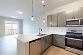Located at 464 Glenwood Ave in Glen Ellyn, Illinois, this well-appointed one-bedroom, one-bathroom residence offers a thoughtfully designed layout with modern finishes throughout. The open-concept kitchen and living area serves as the heart of the home, featuring sleek gray cabinetry, a white quartz peninsula with an undermount sink, a classic white subway tile backsplash, and a full suite of stainless steel appliances including a gas range, built-in microwave, dishwasher, and refrigerator. Stylish pendant lighting illuminates the kitchen, which flows seamlessly into the living area. Light wood-style flooring extends throughout the space, adding warmth and continuity. The spacious primary bedroom features tall ceilings, large sliding glass doors, and direct access to a private balcony overlooking the Glen Ellyn streetscape. The full bathroom is finished with a white vanity, quartz countertop, and a walk-in glass-enclosed shower. A dedicated laundry room houses a full-size washer and dryer, providing added convenience. A connecting hallway ties the rooms together efficiently, completing this clean, contemporary residence designed for comfortable everyday living.