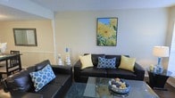 Located in North Richland Hills, this two-story space offers a comfortable and thoughtfully arranged living environment. The living area showcases dark leather sofas accented with blue and yellow throw pillows, creating a vibrant yet cohesive color palette. A glass coffee table anchors the seating arrangement, while a textured area rug adds warmth underfoot. Decorative candle holders and a bold sunflower wall art piece contribute character to the neutral-toned walls. The textured ceiling and clean architectural lines give the space a classic residential feel. The two-story layout provides a sense of vertical space and separation between living and private areas, offering functional versatility for everyday living.