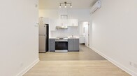 Located at 2238 Rue du Souvenir in Montréal, this efficiently designed one-bedroom unit on the second floor offers a thoughtfully organized layout that maximizes every square metre of available space. The open-concept living and kitchen area forms the heart of the unit, finished with light wood-toned flooring that carries a bright, cohesive feel throughout. The kitchen is well-appointed with two-tone cabinetry — white upper cabinets paired with grey lower drawers — complemented by a white tile backsplash, stainless steel appliances including a refrigerator and electric range, and a range hood. Track lighting overhead and a wall-mounted mini-split air conditioning unit add practical functionality. The bedroom is a compact, quiet space with crisp white walls, light flooring, and a window that introduces natural light. The bathroom features a full soaking tub with large-format white subway tile surround, a toilet, and a window for ventilation and natural light, finished with neutral floor tiles. The overall aesthetic is clean and minimalist, with white walls and light finishes creating a bright, airy ambiance throughout the unit.