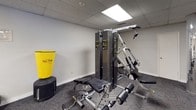 This fitness center offers a comprehensive workout environment designed to support a wide range of exercise routines. The space is laid out on a single floor and features a practical, no-frills aesthetic with carpeted flooring, a drop-panel ceiling with recessed fluorescent lighting, and neutral-toned walls that keep the atmosphere focused and functional.

The cardio section is well-appointed, housing multiple Spirit-brand treadmills and elliptical trainers, along with a recumbent exercise bike — providing ample options for low- and high-impact cardiovascular workouts. A stability ball adds versatility for core training and stretching exercises.

Strength training is supported by a multi-station cable machine with adjustable weight stacks, a dedicated weight bench, and free weights, catering to both resistance and muscle-building routines. A Tae Bo punching bag adds a unique element for those looking to incorporate martial arts-inspired cardio training.

Floor-to-ceiling mirrors line portions of the walls, visually expanding the space and allowing users to monitor their form during workouts. Decorative framed prints, including travel-themed artwork, contribute a modest touch of character to the otherwise utilitarian setting. The center is well-lit and thoughtfully organized to maximize usability across its footprint.