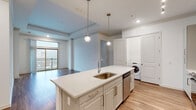 Located at 2925 Buford Dr in Buford, Georgia, this single-floor unit offers a thoughtfully designed open-concept layout with contemporary finishes throughout. The kitchen serves as a central focal point, anchored by a large island with a quartz countertop, undermount sink, and pendant lighting above. White shaker-style cabinetry lines the walls alongside a hexagonal tile backsplash, and stainless steel appliances—including a range, over-the-range microwave, and French door refrigerator—complete the space. An in-unit washer is conveniently positioned nearby. Light wood-tone flooring flows through the kitchen and living areas, while a large sliding glass door opens to a private balcony, bringing in natural light and outdoor views. The bedrooms are carpeted and feature ceiling fans and generously sized windows that overlook the surrounding area. The bathrooms are finished with clean, modern details: one includes a glass-enclosed walk-in shower with tile surround, while another features a soaking tub set within full-height stone-look tile walls. The overall ambiance is bright, neutral, and move-in ready.