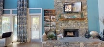 This thoughtfully designed single-floor residence showcases a seamless open-concept layout that connects the key living areas with ease and flow. The communal lounge or clubhouse area makes a striking first impression with soaring ceilings painted in a bold sky blue, elegant arched doorways, and a full kitchen equipped with stainless steel appliances, gray cabinetry, subway tile backsplash, and a bar-height island accommodating multiple stools — ideal for casual dining or socializing. Natural light pours in through large French doors that lead to an outdoor area, enhancing the welcoming atmosphere. The private living space features light wood-look flooring throughout, adding warmth and continuity. The living room offers ample space for comfortable seating, a wall-mounted TV, and French doors that frame views of lush greenery. Crown molding and a ceiling fan add refined finishing touches. The dining area is a cozy, well-defined space with track lighting and room for a full dining set. The kitchen within the private unit features pendant lighting over a curved island with bar seating, white cabinetry, and modern stainless steel appliances. The overall ambiance is contemporary, bright, and inviting throughout.