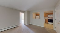 This single-floor residence at 25 English in Manchester, New Hampshire offers a practical and well-organized layout across its living spaces. The spacious living room is carpeted in neutral tones and features a baseboard heating system, with a sliding glass door that opens to a balcony and brings in generous natural light alongside leafy outdoor views. A pass-through window connects the living area to the kitchen, creating an open sightline between the two spaces.

The kitchen is efficiently designed with warm oak cabinetry, light-toned laminate countertops, and a tile backsplash. It is equipped with a full suite of appliances including a refrigerator, electric range, dishwasher, and over-the-range microwave, with tile flooring completing the space.

The bedroom is generously sized, featuring plush carpeting, a reach-in closet, and a window framing natural wooded views, adding a calm, private atmosphere. Baseboard heaters are present throughout the unit for consistent warmth.

The bathroom includes a full tub-shower combination with a clean white surround, a toilet, and a wood-toned vanity with a countertop sink, all finished with light tile flooring. Overall, the unit presents a functional, comfortable layout with consistent neutral finishes throughout.