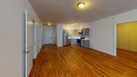 This 2-bedroom, 1-bathroom residence at 6035 Park Ave in West New York, NJ offers a well-designed, single-floor layout that balances modern finishes with functional living spaces. Rich hardwood flooring flows throughout the unit, lending warmth and continuity to every room.

The open living area is generously proportioned, featuring large windows that allow natural light to fill the space and offer views of the surrounding neighborhood. The room provides ample space for flexible furniture arrangements.

The kitchen is outfitted with a full suite of stainless steel appliances, including a refrigerator, electric range, microwave, and dishwasher. Contemporary gray cabinetry extends to the ceiling for abundant storage, while white countertops and a classic subway tile backsplash complete the clean, modern aesthetic. The kitchen opens naturally toward the living area, creating a connected feel.

Both bedrooms continue the hardwood flooring and offer neutral walls ready for personalization. One bedroom features a window with an exterior view and a wall-mounted HVAC unit for individual climate control.

The bathroom is finished with wood-plank style tile flooring, a modern vanity with ample counter space, a large mirror, and accessibility grab bars for added convenience. A frosted glass door leads to a separate area, enhancing privacy within the space.