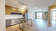Located on Dyke Lane in Stamford, Connecticut, this well-appointed one-bedroom, one-bathroom residence offers a thoughtfully designed open-concept layout finished with light hardwood-style flooring throughout. The combined kitchen and living area forms the heart of the home, where a sleek, modern kitchen impresses with textured wood cabinetry, gray lower cabinets, white countertops, a full suite of stainless steel appliances including a gas range, microwave, dishwasher, and French door refrigerator, complemented by track lighting overhead. The open living area flows seamlessly from the kitchen, offering generous space bathed in natural light. The bedroom features a large floor-to-ceiling window with urban views and access to a private balcony with city scenery, creating a bright and airy atmosphere. A dedicated closet with wire shelving provides practical storage. The bathroom is elegantly appointed with a dual-sink vanity, modern flat-panel cabinetry, backlit mirrors, and a stacked in-unit washer and dryer conveniently integrated within the space. Clean neutral tones and contemporary finishes lend the entire residence a cohesive, modern aesthetic suited for comfortable Stamford living.