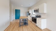 This 500 square foot apartment, located at G1-202, offers a well-designed living space that maximizes functionality. The single-floor layout comprises one bedroom, one bathroom, and an open-concept kitchen and living area. The primary bedroom, measuring 150 square feet, provides ample space and features a large window that allows natural light to flood the room, enhancing its airy feel.

The modern bathroom is outfitted with a white vanity, providing storage and counter space. It includes a toilet, bathtub, and is finished with warm wood-look flooring that extends throughout the apartment, creating a cohesive aesthetic.

The kitchen is a highlight, featuring sleek white cabinetry, stainless steel appliances, and a subway tile backsplash. A central island with a butcher block top adds extra preparation space and casual dining options. The teal blue door adds a pop of color, contrasting nicely with the neutral palette.

Large windows in the living areas and bedroom offer views of the surrounding area and fill the space with natural light. The apartment's design emphasizes clean lines and a bright, open feel, making it an ideal living space for those seeking a modern, low-maintenance home in an urban setting.