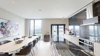 Located at 70 Ordnance Street in Toronto's vibrant King West neighbourhood, this elegantly designed amenity space spans a single floor and offers a refined blend of modern aesthetics and functional comfort. The space is divided into a living room and a dining room, each thoughtfully appointed with upscale furnishings and cohesive design elements throughout.

The living room is a bright, inviting retreat anchored by plush velvet sofas and sculptural lounge chairs arranged around a marble-topped coffee table. Floor-to-ceiling windows and glass-panel doors flood the room with natural light while framing sweeping panoramic views of the Toronto skyline and surrounding cityscape. Curated artwork adorns the textured walls, adding a vibrant artistic touch to the neutral palette of light hardwood flooring and soft grey tones.

The dining area is equally impressive, featuring a long communal table with contemporary leather chairs, complemented by a built-in banquette nook with dramatic pendant lighting and open display shelving. Adjacent to the dining space, a fully equipped kitchen showcases striking dark marble backsplash and countertops, a large island with bar seating, and sleek cabinetry — creating a seamless environment ideal for gatherings and entertaining. Together, these spaces deliver a polished, hotel-inspired ambiance suited to a premier Toronto address.