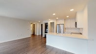 This single-floor residence showcases a clean, contemporary design throughout. The open-concept layout seamlessly connects the kitchen and living area, creating a generous and versatile living space anchored by rich hardwood-style flooring. Recessed lighting illuminates the area, while large black-framed windows invite abundant natural light and offer views of the surrounding cityscape.

The kitchen is well-appointed with white shaker cabinetry, quartz countertops, a classic subway tile backsplash, and a full suite of stainless steel appliances including a refrigerator, range, over-the-range microwave, and dishwasher. A peninsula with an undermount sink provides additional prep space and casual seating. Tucked conveniently off the main living area is an in-unit stacked washer and dryer closet.

The bedroom features plush carpet flooring, a large black-framed window with city views, and an exposed duct detail that adds an industrial design accent. The bathroom is finished with light tile flooring, a dark-toned vanity with ample storage, a quartz countertop, an illuminated LED mirror, and a glass-enclosed shower. The overall aesthetic of the space is modern and cohesive, combining neutral tones with functional, high-quality finishes throughout.