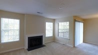 Located in Sterling, Virginia, this single-floor home at Ridgehaven Terrace offers a welcoming and functional layout. The main living area is a highlight of the space, featuring a classic white-trimmed fireplace with a sleek dark hearth that serves as a natural focal point. Neutral beige walls and light-toned carpeting create a warm, understated palette throughout. Two generously sized windows allow ample natural light to fill the room, with views of the surrounding outdoor greenery, lending the interior an open and airy feel. A sliding door or additional window panel on the side wall further enhances brightness and provides additional access to the outdoors. The smooth white ceiling with recessed lighting adds a clean, finished look to the space. The overall ambiance is calm and move-in ready, with a neutral design scheme that accommodates a variety of interior styles. The home's single-floor layout offers convenient accessibility and ease of movement throughout.