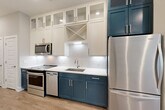 Located at 2550 Blackmon Dr in Decatur, GA, this efficiently designed single-floor unit makes thoughtful use of its intimate footprint. The kitchen is a standout feature, showcasing a bold two-tone cabinet scheme with navy lower cabinets and white upper cabinets — including glass-front and X-detail display sections. A textured white tile backsplash, white quartz countertops, stainless steel appliances, and recessed lighting complete the well-appointed culinary space. Light wood-style flooring runs throughout, creating a cohesive and airy feel as the kitchen flows into the living area. The living room benefits from generous natural light through a set of glass double doors and a side window, both framing views of surrounding greenery. An additional room with a window provides flexible living or workspace. The walk-in closet offers dual shelving and hanging rods on both sides, providing ample storage capacity. Two bathrooms serve the unit: one features a navy vanity with a white quartz top and an octagonal mirror, while the other includes a glass-enclosed walk-in shower with marble-toned tile walls and a mosaic tile floor. Neutral warm-beige walls and clean white trim throughout lend the space a fresh, modern aesthetic.